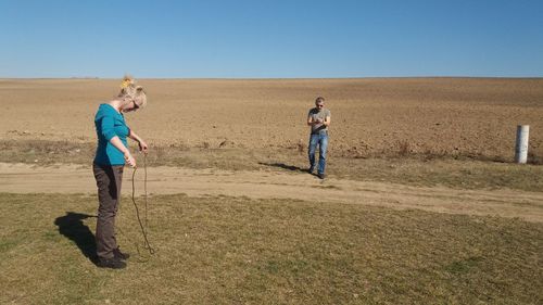 Woman looking at jumping rope while man walking on grassy field against clear sky