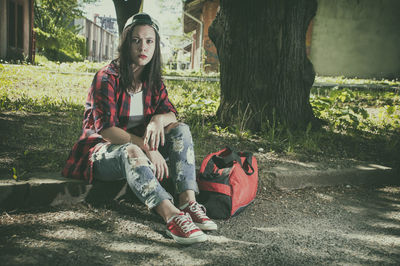 Young woman sitting by bag on field