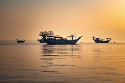 Fishing boats in sea against sky during sunset