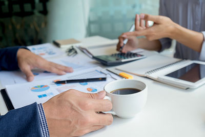 Close-up of woman using coffee cup on table