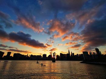 Silhouette cityscape by sea against sky during sunset