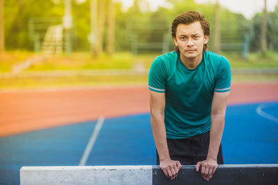 Portrait of young man standing behind hurdle on running track