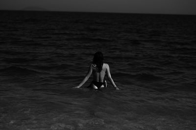 Low section of woman sitting at sea shore against sky