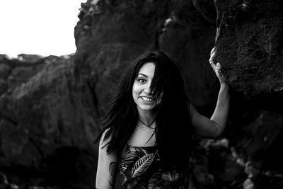 Portrait of smiling young woman standing by rock formations