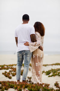 Mixed race couple embracing on sand dunes maternity