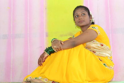 Portrait of young woman standing against yellow wall