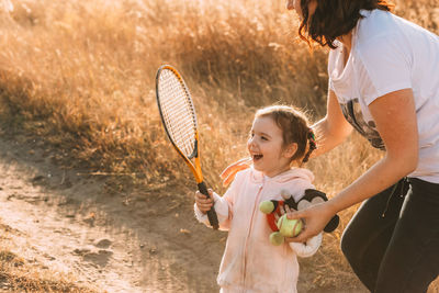 Cute little girl is enjoying a tennis racket in her hand. mom hands her a tennis ball