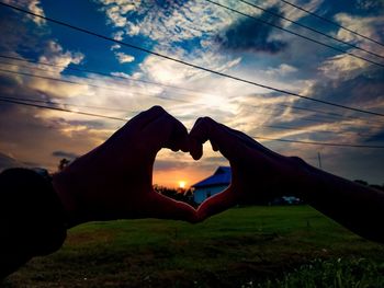 Midsection of man holding heart shape against sky during sunset