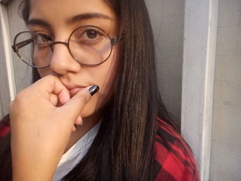 Close-up portrait of thoughtful young woman wearing eyeglasses against wall