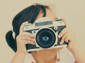 Close-up of girl photographing through camera against white background