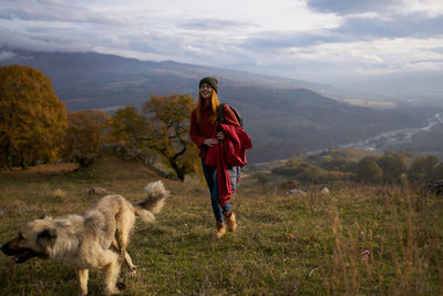 Full length of man with dog standing on mountain against sky