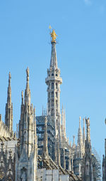 Low angle view of statue at milan cathedral against blue sky