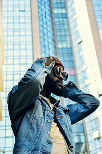 Low angle view of man wearing sunglasses while standing against modern buildings in city