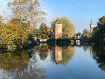 Bridge over river amidst trees and buildings against sky