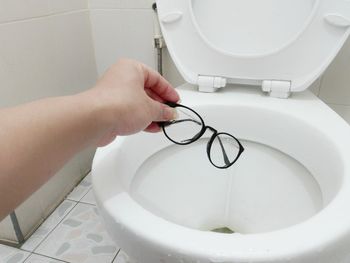 Cropped hand of woman putting eyeglasses in toilet bowl