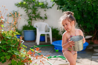 Cute young girl watering plants with a bucket on a summer day in the backyard