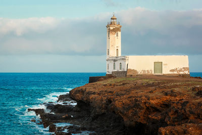 Lighthouse by sea against sky