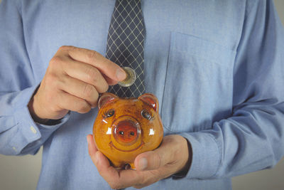 Midsection of businessman putting coin in piggy bank