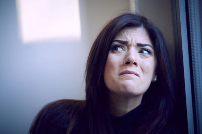 Close-up of worried woman looking away by window