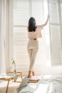 Rear view of woman standing on bed at home