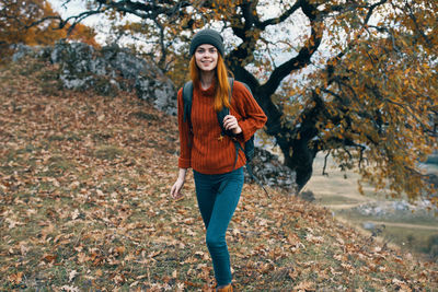 Portrait of smiling young woman standing in autumn tree
