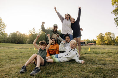 Portrait of cheerful kids screaming with counselors on grass in playground at summer camp