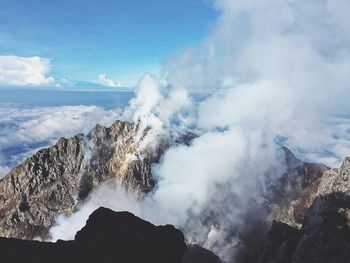 High angle view of smoke emitting from mountain against sea and cloudy sky