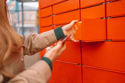 Midsection of person holding mobile phone against orange wall