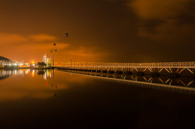 Low angle view of overhead cable car by bridge on sea at night