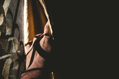 Cropped hand of person holding curtain in darkroom