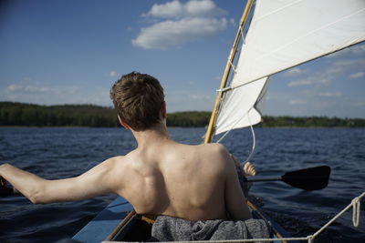 Rear view of shirtless man sailing in sea against sky