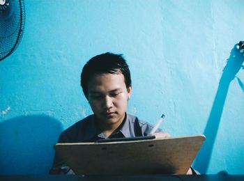 Portrait of young man using mobile phone against wall