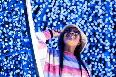 Joyful woman of color with a white beanie braided hairstyle and pink glasses enjoying the christmas 