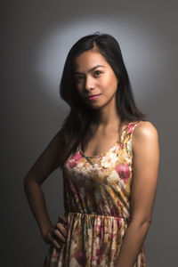 Portrait of young woman standing against gray background