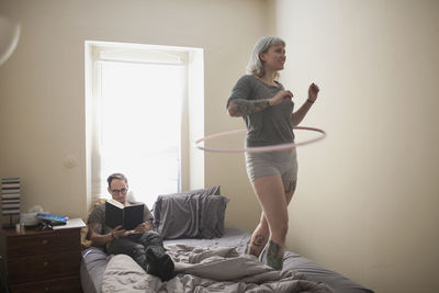 Young woman standing on bed doing hula hoop