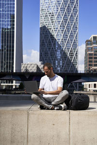Man using laptop in front of buildings on sunny day