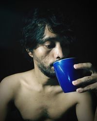 Portrait of young man drinking glass against black background