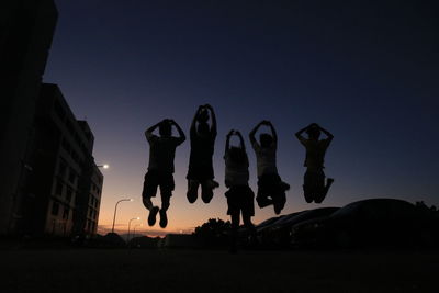 Low angle view of people jumping against sky at night