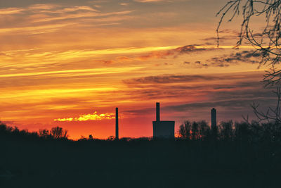 Silhouette of factory against sky during sunset