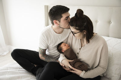 Tattooed millennial dad kisses mom while she holds their newborn