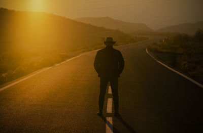 Silhouette of adult man in cowboy hat standing on country road during sunset. almeria, spain