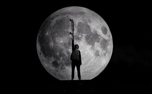 Rear view of man standing against moon at night