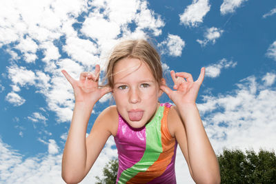 Portrait of happy girl with arms raised against sky