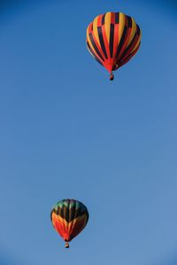 Low angle view of hot air balloons flying in clear blue sky