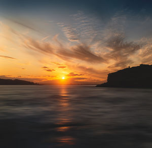 Long exposure wide angle of a dramatic coastal sunset with silhouette of a light house on a cliff