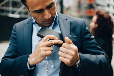 Mature businessman positioning mobile phone and in-ear headphones in suit pocket