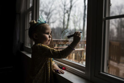 Side view of girl drawing on window