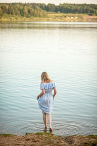 A slender blonde girl in a summer dress enters the river on a summer evening. summer vacation. 