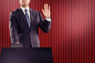 Midsection of male politician taking oath at podium against red curtain