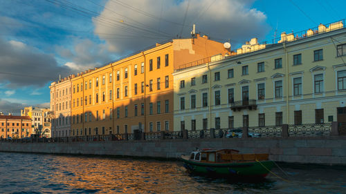 Boats in river by buildings in city against sky